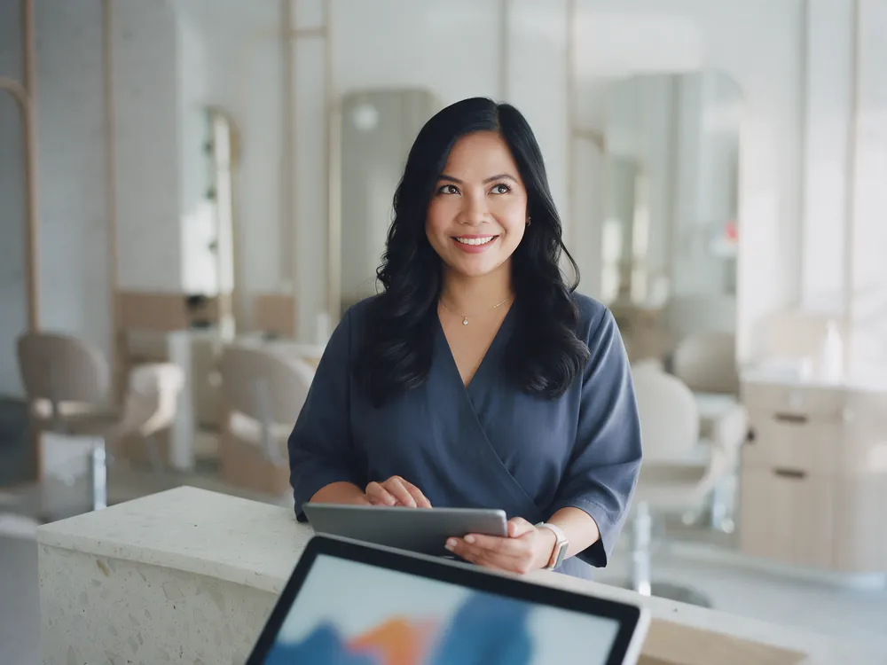 A salon owner at her reception desk, smiling, with a tablet in hand